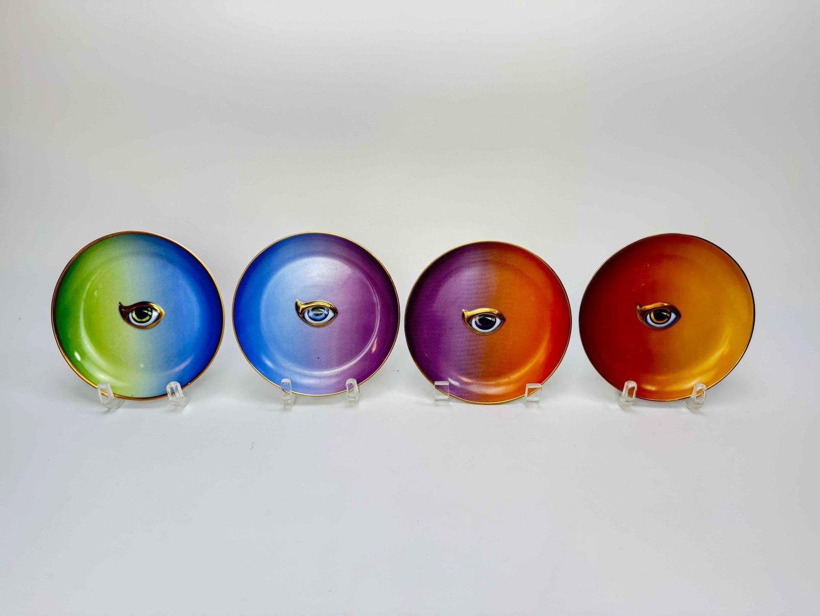 SET OF 4 L'OBJET LITOOMBRE EYE MOTIF PORCELAIN DISHES: Set of 4 ombre orange and violet porcelain dishes with surrealist eye motif and gilt rims Approximate Dimensions: 6"Dia. Artist or Maker: L'Objet 'Lito' Provenance: A New York Galleris
