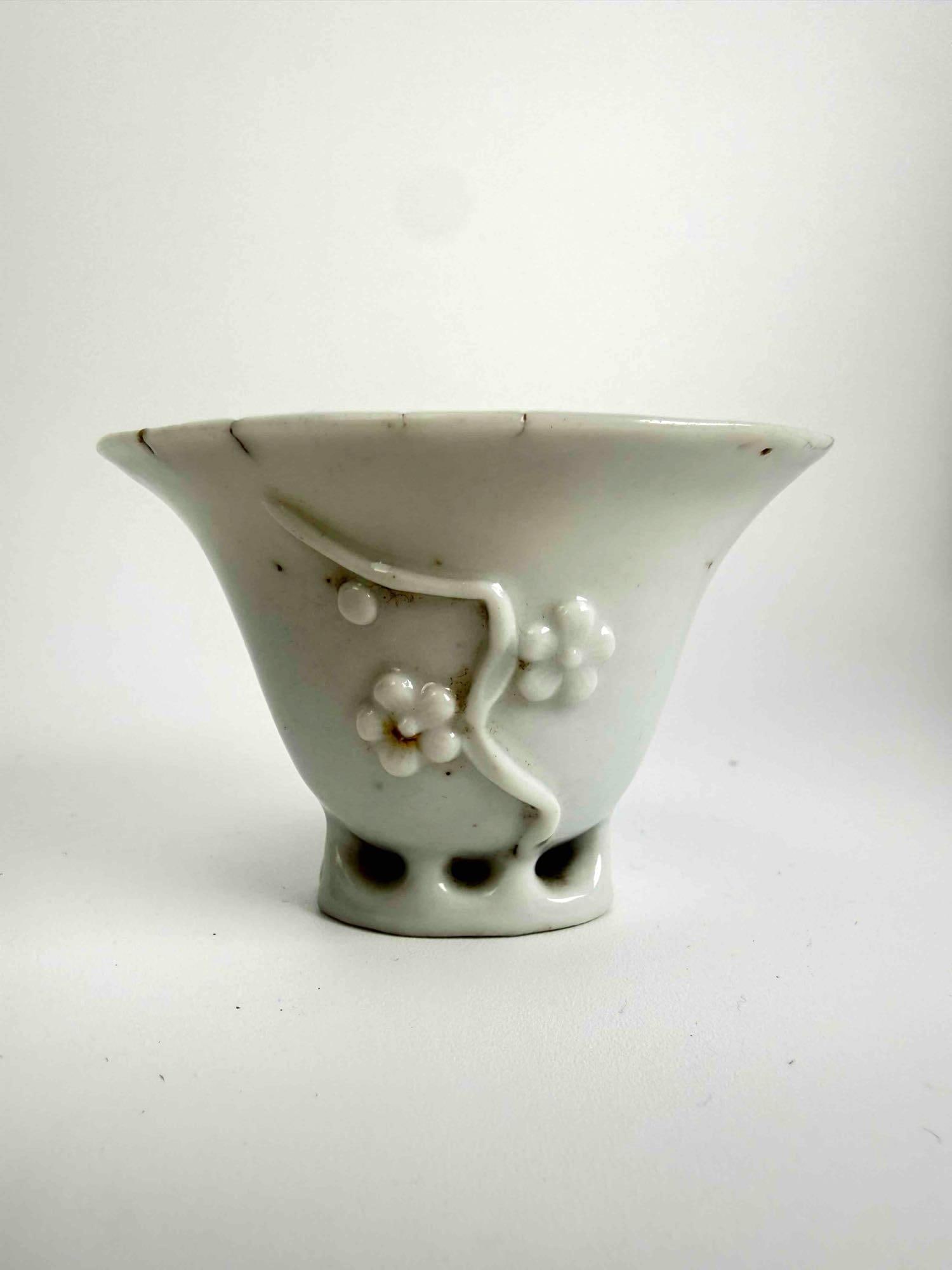 MING DYNASTY DEHUA "BLANC DE CHINE" PORCELAIN LIBATION CUP, PRUNUS/PLUM BLOSSOM RELIEF: Rare antique 17th-century Chinese Ming Dynasty molded Dehua "Blanc de Chine" porcelain libation cup having a flared rhinoceros horn form rim adorned with delicate sprigs of flowering prunus pl