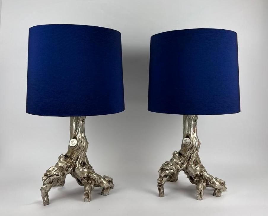 PAIR OF SILVERED TREE TRUNK FORM TABLE LAMPS WITH BLUE SHADES: Pair of table lamps, each cast as a naturalistic tree trunk and root form in a bright silvered finish, fitted with navy blue drum shades, Note: One of the finials has been repaired with adhesive; orb