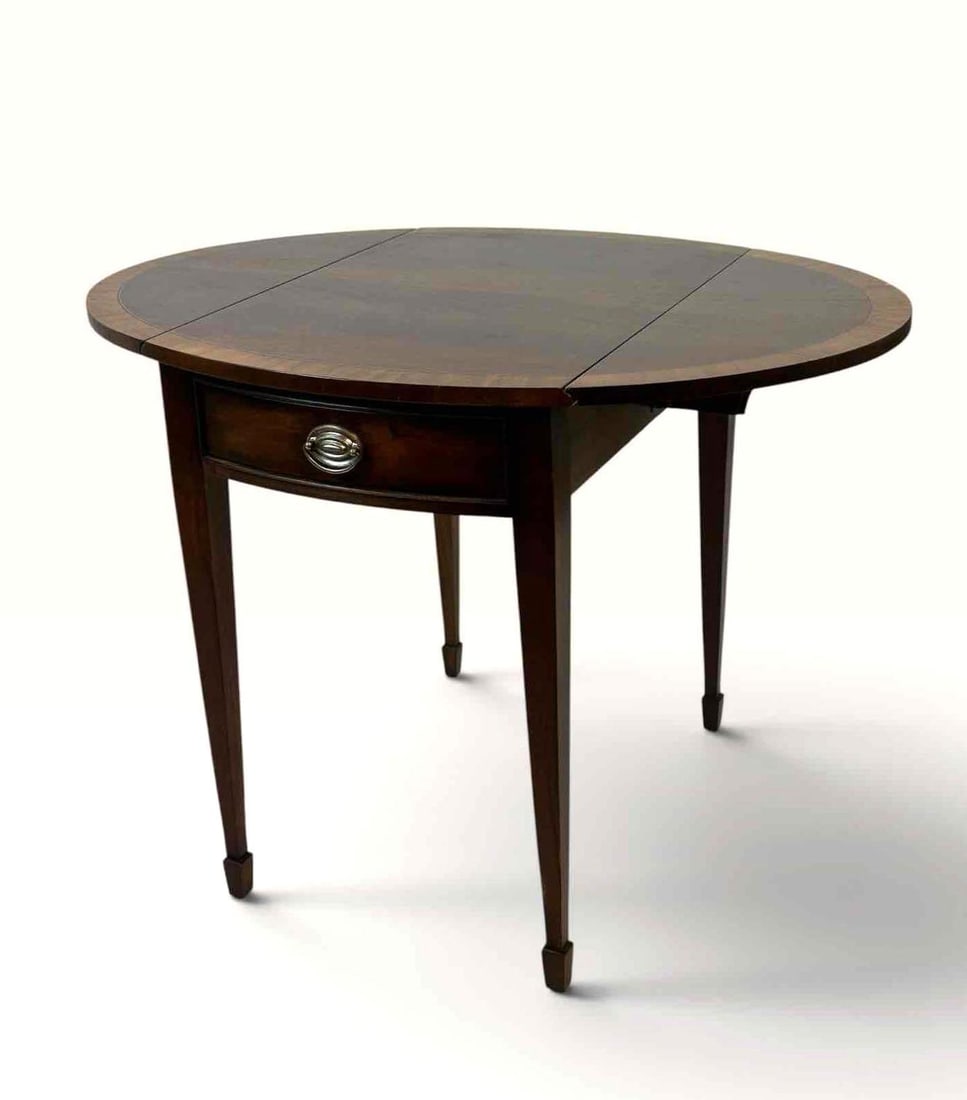 ETHAN ALLEN MAHOGANY DROP LEAF PEMBROKE TABLE: Drop leaf table with a figured mahogany top and crossbanded border, photographed with the leaf lowered, raised on square tapered legs with brass cap feet Approximate Dimensions: 37 x 28 x 28" Arti