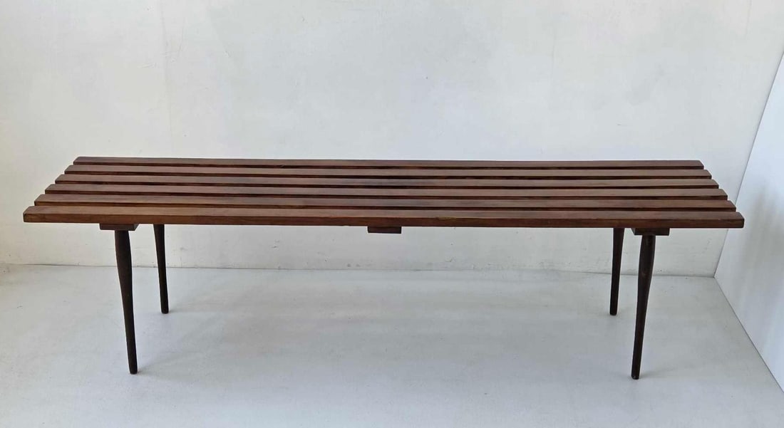 MID CENTURY MODERN WOOD SLAT BENCH WITH TAPERED DOWEL LEGS: Long low slat bench in stained hardwood with shaped slat top, tapered dowel legs, and an impressed MADE IN mark to the underside Approximate Dimensions: 15.75" H x 60" W x 16.75" D Artist 
