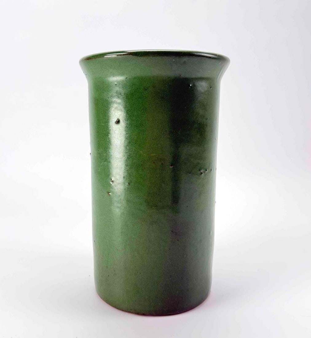 GREEN GLAZED CERAMIC CYLINDER VASE: Cylindrical ceramic vase in a mottled green glaze running to darker tones at the shoulder, with a slightly everted rim Approximate Dimensions: 9.25" H x 5.75" Dia Artist or Maker: Unknown Prov
