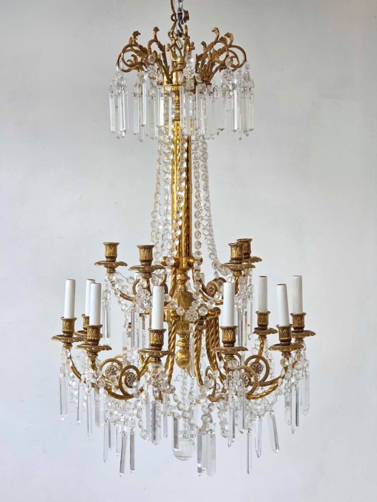 GILT BRONZE AND BOHEMIAN CRYSTAL CHANDELIER, SKLARNY BYDZOV CRYSTAL LABEL: Gilt bronze chandelier hung with Bohemian crystal, scrolled arms with fluted candle sockets, faceted crystal button chains, prism drops and faceted ball drop, with gold foil crystal label to one prism