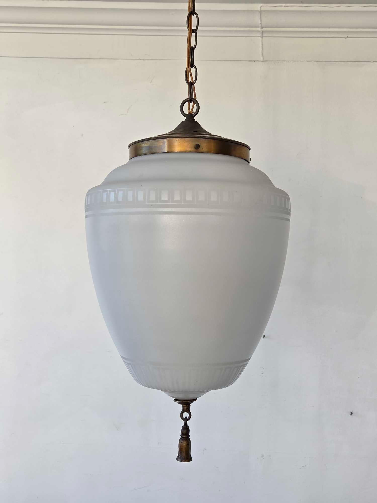 LARGE WHITE GLASS PENDANT FIXTURE WITH BRONZE TASSEL DETAIL: Large frosted white glass pendant light of urn form, moulded panel band at the shoulder and ribbed lower body, patinated bronze collar with suspension chain, and cast bronze tassel drop Approximate