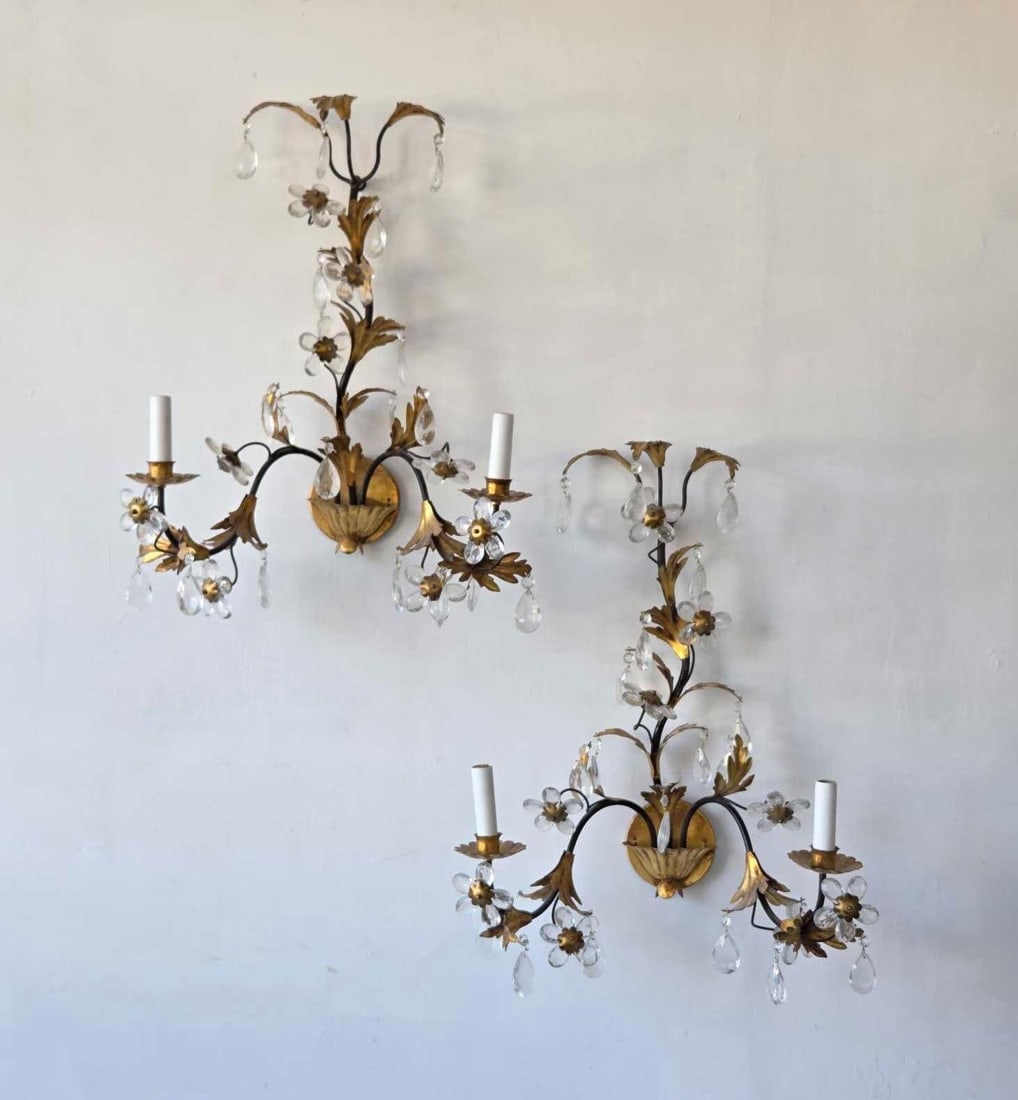 PAIR OF GILT METAL AND CRYSTAL TWO LITE SCONCES: A pair of two light wall sconces in gilt metal, each with a leafy branching frame hung with crystal flowerheads and faceted prism drops above a shaped gilt backplate Approximate Dimensions: 23" H