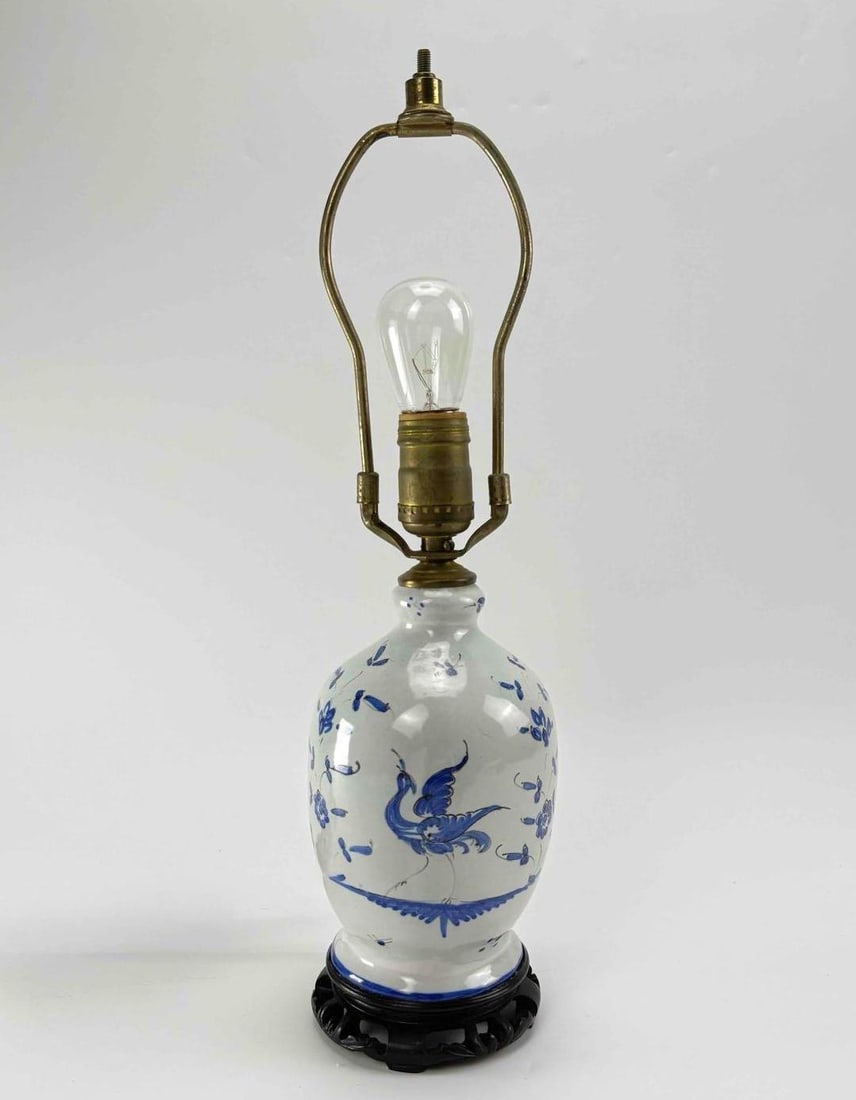 BLUE AND WHITE PORCELAIN TABLE LAMP ON CARVED WOOD BASE: Table lamp with an ovoid blue and white porcelain body painted with birds among flowering branches, with brass cap, socket and harp, raised on a turned dark wood base Approximate Dimensions: 17.25"