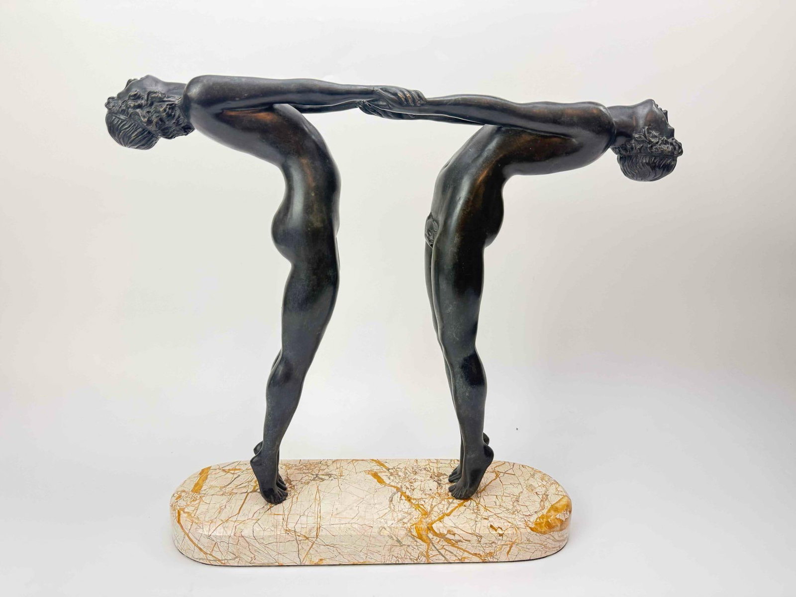 ART DECO STYLE BRONZED SCULPTURE OF TWO DANCERS ON MARBLE BASE: Art Deco style sculpture of two stylized nude dancers standing back to back and arching outward with joined hands, in a dark bronzed finish, raised on a shaped variegated marble base Approximate
