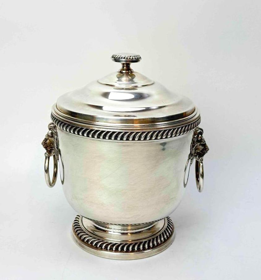 SILVER PLATED LION MASK ICE BUCKET WITH GADROONED BORDERS: Urn form silver plated ice bucket with lion mask and ring handles, gadrooned rim and foot borders, and a domed cover with turned finial Approximate Dimensions: 10" H x 8" Dia Artist or Maker: 