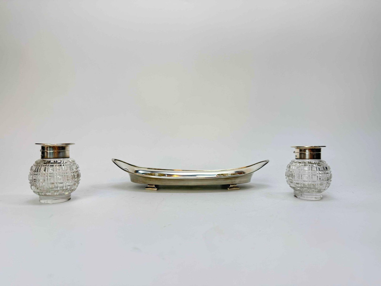 GEORGE V SILVER MOUNTED CUT GLASS INKSTAND BY JOHN GRINSELL & SONS, BIRMINGHAM 1914: Sterling silver mounted cut glass inkstand, comprising a pair of cut glass inkwells with hinged silver mounted covers, together with a sterling silver mounted footed tray of navette form; the tray hal