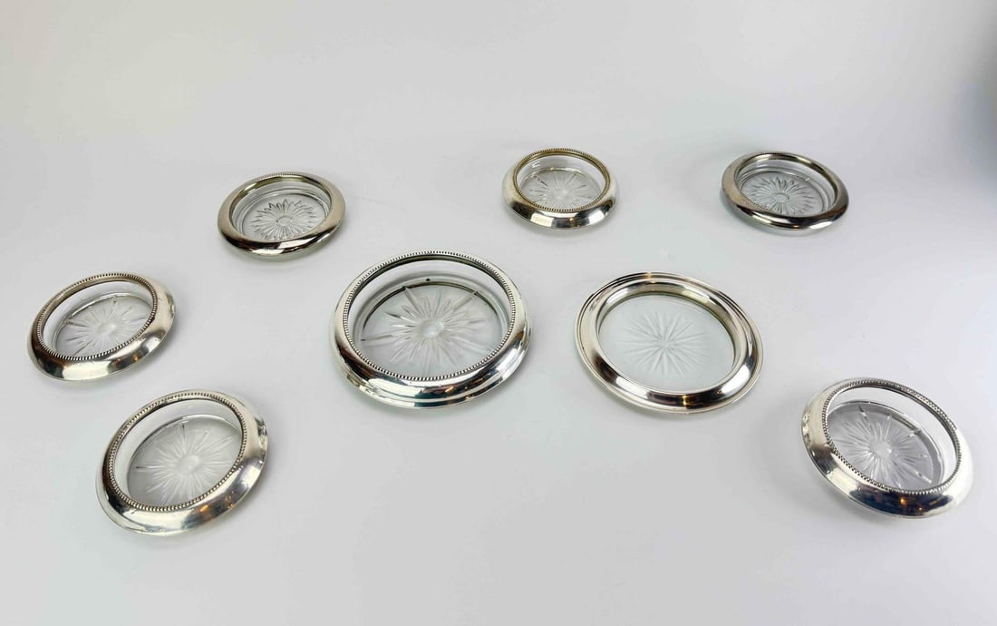 SET OF EIGHT FRANK M. WHITING STERLING RIMMED CUT GLASS COASTERS: Set of eight coasters with pressed and cut glass inserts of radiating starburst design set within beaded sterling silver rims, comprising one larger bottle coaster and seven smaller drink coasters App