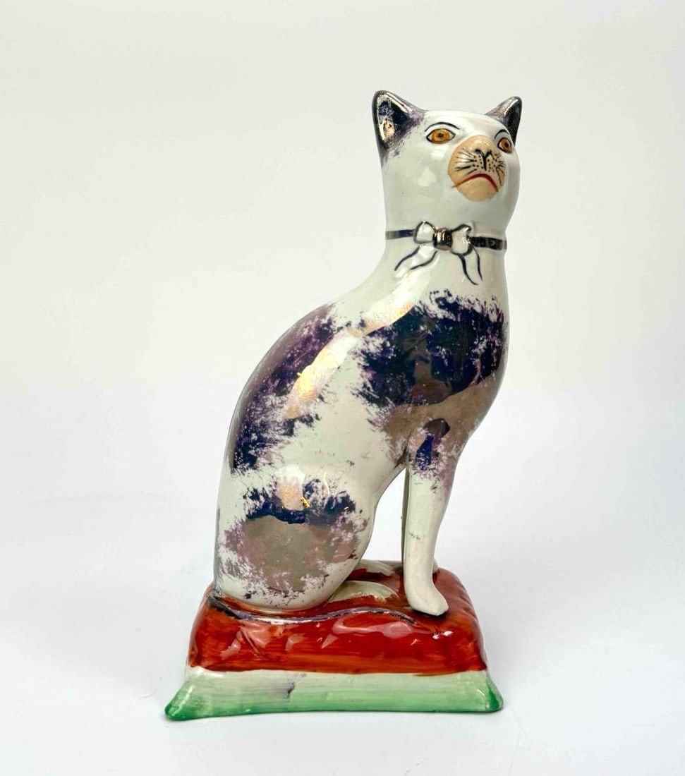 OLD STAFFORDSHIREWARE POTTERY CAT FIGURE ON A TASSELLED CUSHION: Pottery figure of a seated cat Approximate Dimensions: 7.25 "H x 3.5 "W Artist or Maker: Old Staffordshireware Provenance: From a New York Collector Notes: Although care is taken to photograph