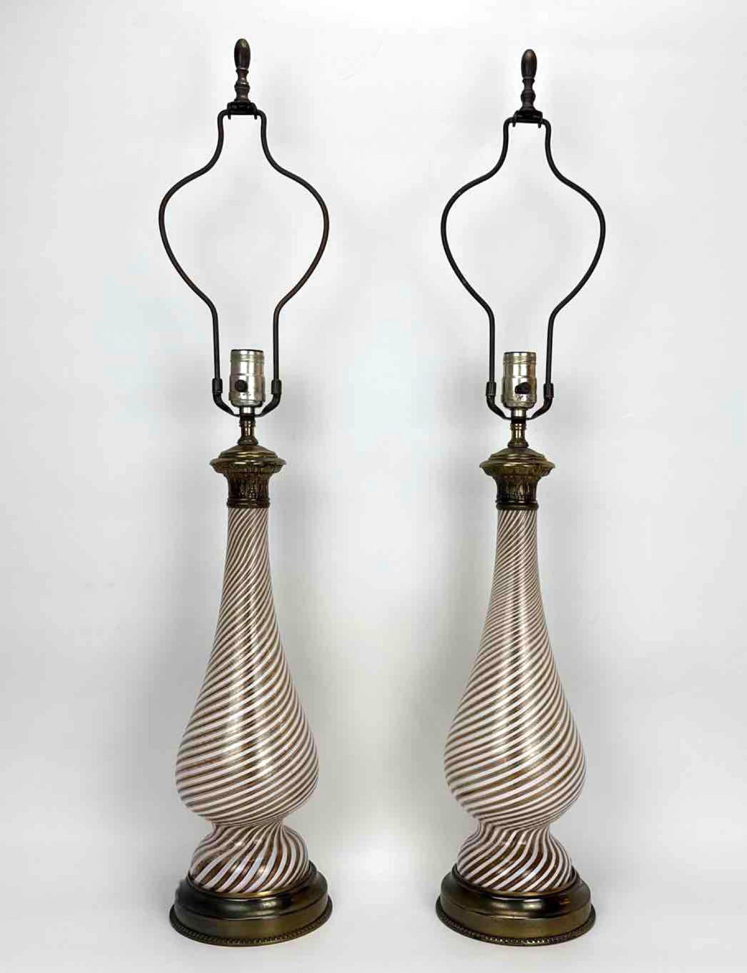 PAIR OF MURANO STYLE WHITE LATTICINO AND GOLD AVENTURINE SWIRL GLASS TABLE LAMPS: Pair of blown glass baluster table lamps, white latticino ribbons alternating with gold aventurine swirl, mounted on gilt brass beaded circular bases with cast foliate capitals Approximate Dimensions: