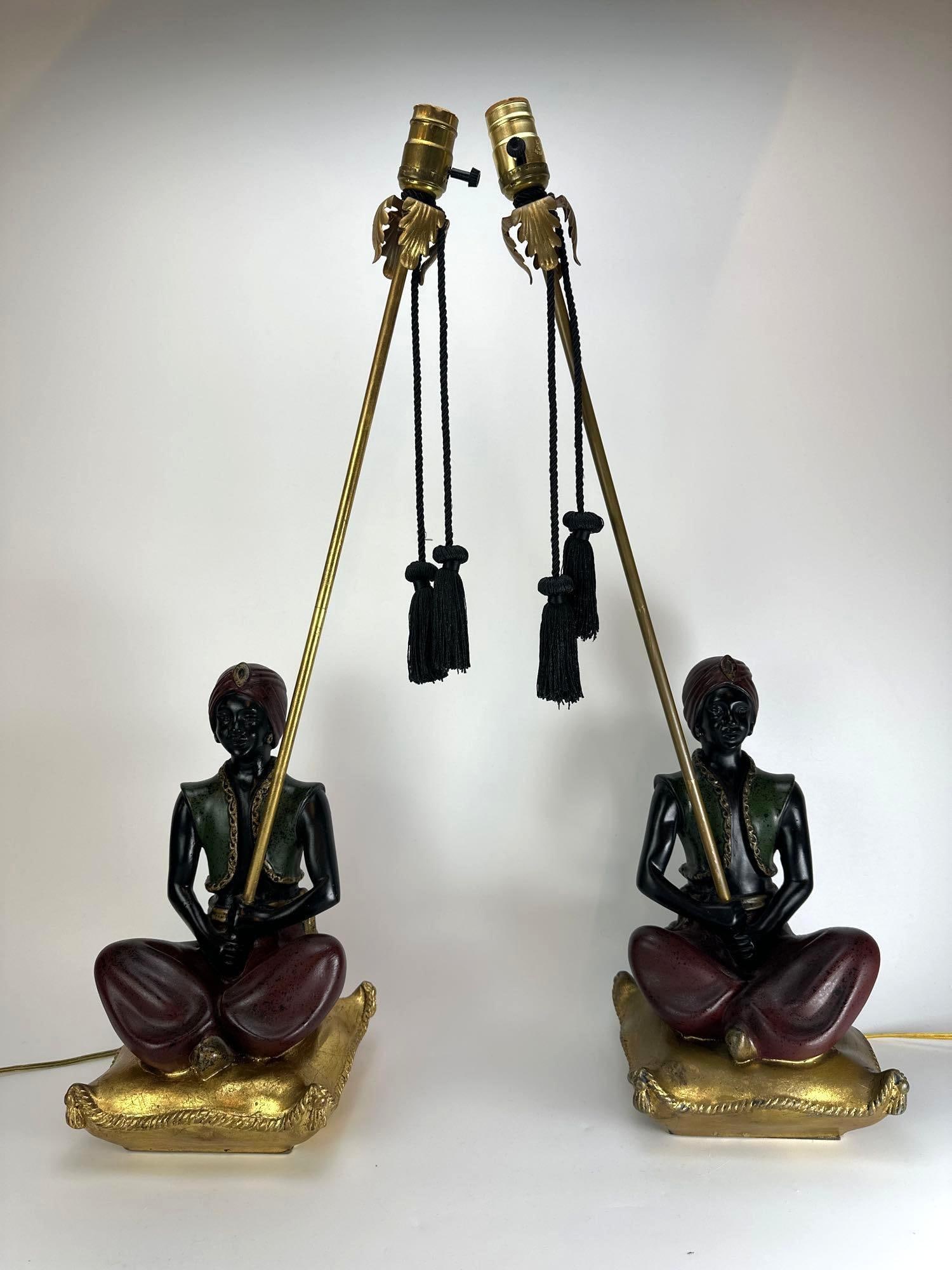 PAIR OF MID CENTURY MOORISH GENIE TABLE LAMPS: Pair of Orientalist figural table lamps, seated robed figures on gilt cushion bases with slender brass stems and black tapered shades Approximate Dimensions: 28.5" H x 12" W x 11" D Artist
