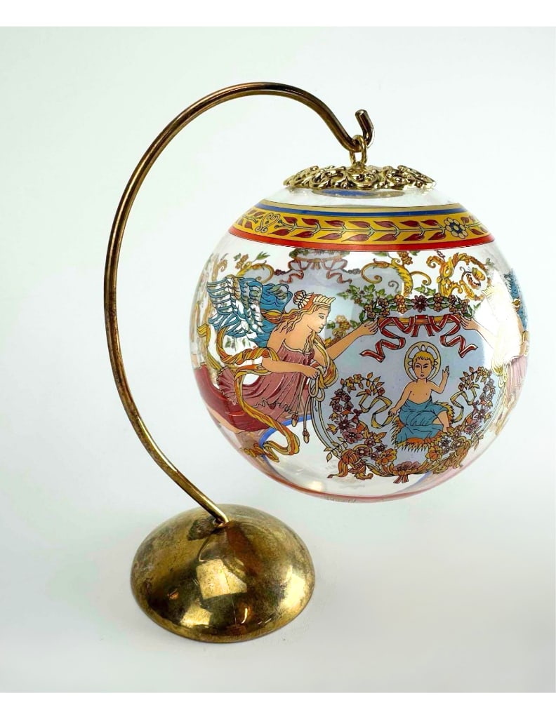 VERSACE BY ROSENTHAL ORNAMENT ON STAND: Spherical glass ornament decorated with classical figures within Greek key and floral borders, suspended from an arched brass display stand Approximate Dimensions: 6" H x 5" W x 4" D Artis