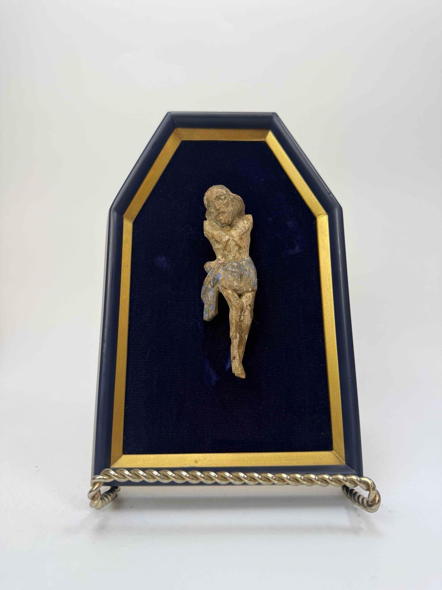 CARVED WOOD CORPUS CHRISTI FIGURE, MOUNTED ON A VELVET LINED DISPLAY PANEL: Carved wood corpus with traces of gesso and polychrome, the head inclined and knees drawn, arms lacking, mounted on a shaped blue velvet lined panel with a gilt fillet surround and a rope twist metal 
