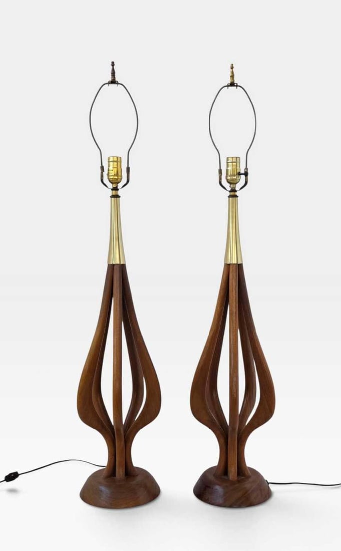 PAIR OF MID CENTURY WALNUT AND BRASS TABLE LAMPS: Pair of mid-century modern table lamps with sculpted open walnut bodies and brass mounts, raised on turned walnut bases, with harps (no shades) Approximate Dimensions: 30.5” H X 8” W X 8” D; Har