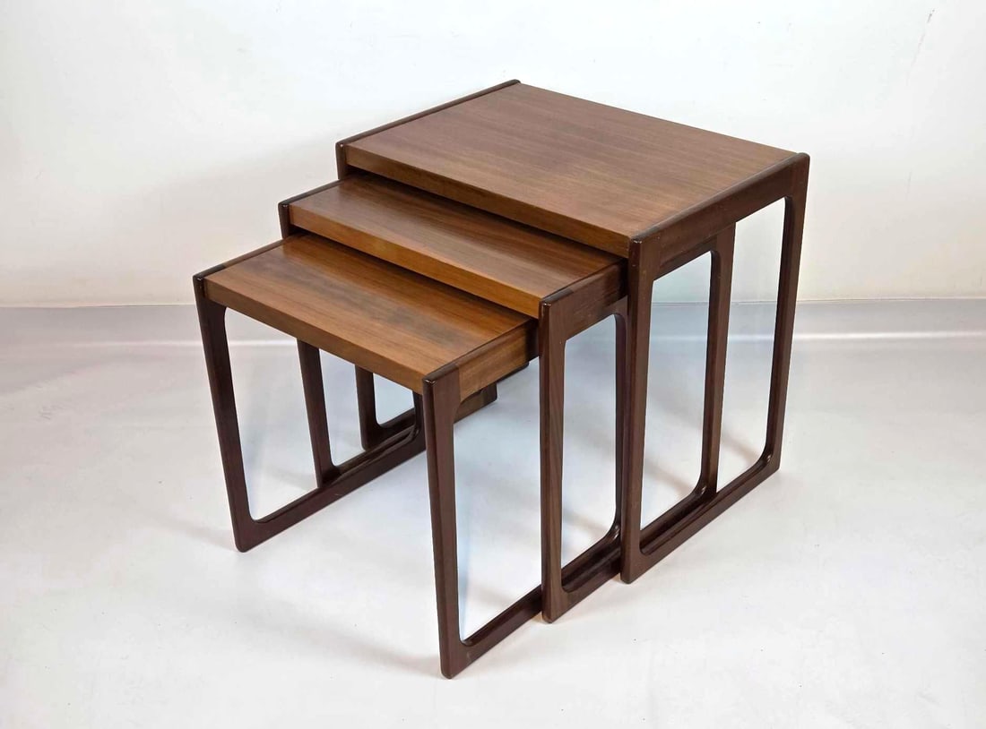 DANISH MID CENTURY WALNUT NESTING TABLES IN THE MANNER OF KAI KRISTIANSEN: A set of three nesting mid-century modern walnut side tables with contoured open sled frames. Approximate Dimensions: 22.25" H x 23.5" W x 16.5" D Artist or Maker: Unknown Provenance: A Ne