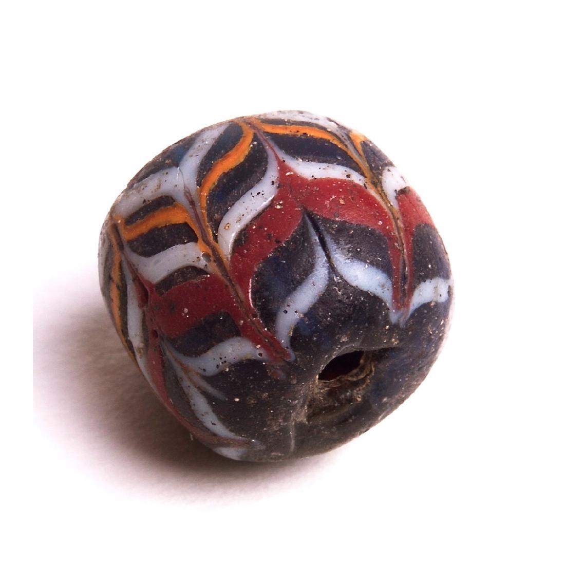 Ancient Islamic Mosaic Glass Bead c.1000 AD.: Ancient Islamic Mosaic Glass Bead c.1000 AD. Size 13 mm. Dark Glass with feathers pattern of white yellow and red glass. Condition: perfect as seen in image. Provenance: Ex Tom Cederlind Estate Oregon