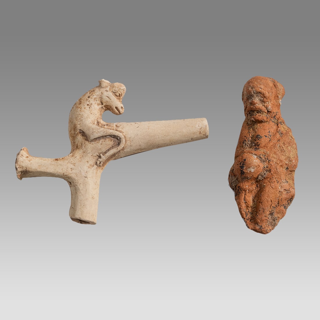 Lot of 2 Greek Terracotta Fragments.: Lot of 2 Greek Terracotta Fragments. Size 2 1/2 - 2 3/4 inches length. A Greek terracotta fragment of Silenos, together with a clay handle with animal fragment from a vessel. Provenance: East Coast Co