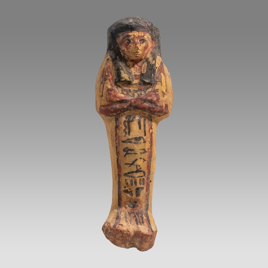 Ancient Egyptian Terracotta Ushabti Ca. late 19th Dynasty, ca. 1295 - 1186 B.C.: Ancient Egyptian Terracotta Ushabti Ca. late 19th Dynasty, ca. 1295 - 1186 B.C. Size 7 1/8 inches high. Molded terracotta ushabti, wearing a black painted royal wig, holding red painted royal implemen