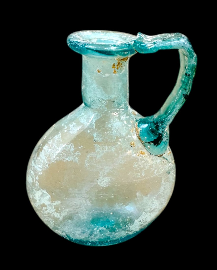 Ancient Roman Glass bottle with one handle – ca 1st – 4th c. AD: Ancient Roman Glass bottle with one handle – ca 1st – 4th c. AD. Size 4 1/2 inches high. Used for scented oils? Modern gold colored wire wrapped around neck. From the collection of Franke Zollman,