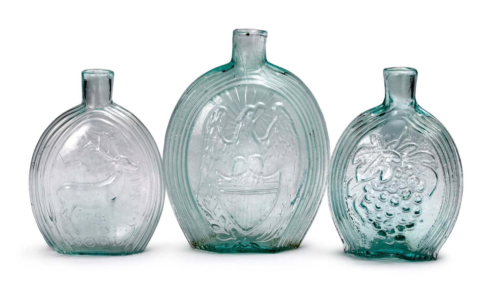Three pale aqua historical glass flasks: Three pale aqua historical glass flasks, mid 19th c., to include an eagle and flag, a deer and willow, and grapes and sheaf of wheat, McKearin GII-53, GX-2, GX-3, 6 1/2'' h., 5 1/2'' h. Provenance: A 
