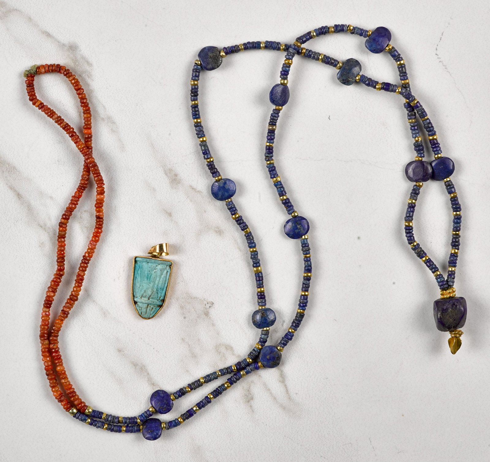 Two pieces of Egyptian jewelry: Two pieces of Egyptian jewelry, to include a turquoise lotus flower pendant with a 14K gold frame, 1'' l. and a lapis lazuli and carnelian mummy bead necklace with 18K gold spacers, 32'' l.