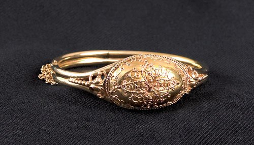 14K yellow gold bangle bracelet, of tubular for: 14K yellow gold bangle bracelet, of tubular form with a top medallion and etruscan design, hinged with a safety chain, 10.3 dwt.
