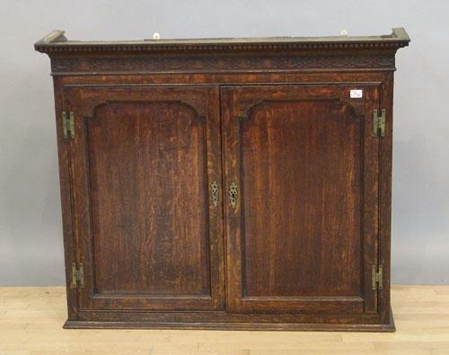 George III oak hanging cupboard top with a dentil: George III oak hanging cupboard top with a dentil molded and blind fretwork cornice and two arched paneled doors, 40 1/2'' h., 44 1/2'' w.