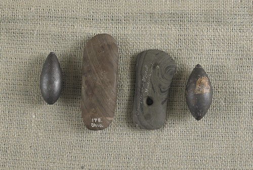 One slate bannerstone, together with a slate pend: One slate bannerstone, together with a slate pendant and two hematite plummets, banner - 4 3/4'' w.