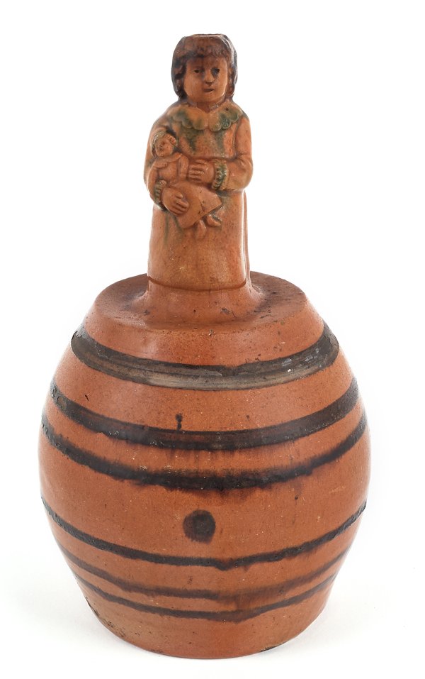 American redware jug, late 19th c., with a figu: American redware jug, late 19th c., with a figural finial of a child holding a doll and manganese bands, 9 1/4'' h.