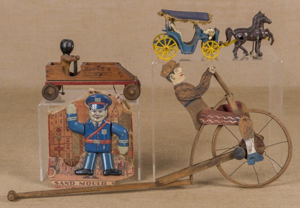 Painted wood bicycle rider push toy, 15'' h., toge: Painted wood bicycle rider push toy, 15'' h., together with a Happy Ham Farm Productions wood pull toy, 9 3/4'' l., a Stanley cast iron horse drawn surrey, 11 1/2'' l., and a Chein tin sand mould.