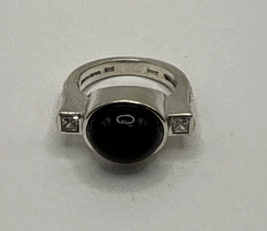 JUDITH RIPKA STERLING SILVER RING WITH OVAL BLACK STONE & COLORLESS STONES: JUDITH RIPKA STERLING SILVER RING WITH OVAL BLACK STONE & COLORLESS STONES Experience the elegance of Judith Ripka with this exquisite sterling silver ring. At its heart lies an oval black stone, comp