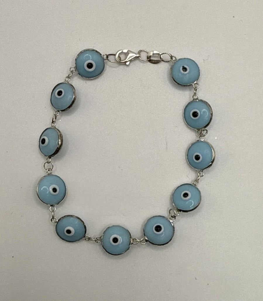 7" EVIL EYE BRACELET: 7" EVIL EYE BRACELET The 7" Evil Eye Bracelet is a stylish and charming piece of fashion jewelry. With a blue color and silver metal, this bracelet exudes a trendy and unique allure. The evil eye desi