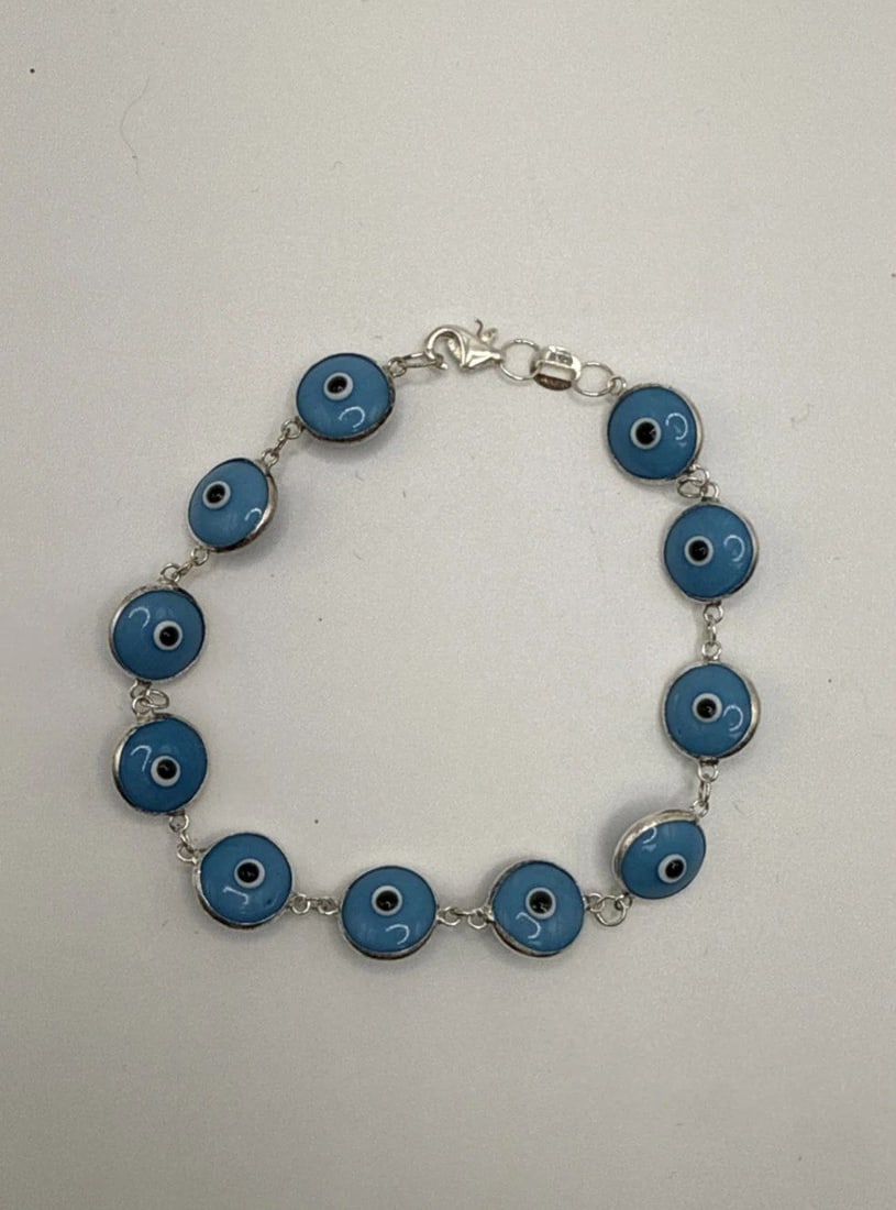 7" EVIL EYE BRACELET: 7" EVIL EYE BRACELET The 7" Evil Eye Bracelet is a stylish and charming piece of fashion jewelry. With a blue color and silver metal, this bracelet exudes a trendy and unique allure. The evil eye desi