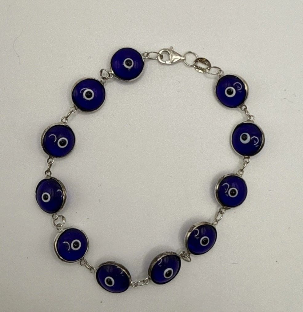 7" EVIL EYE BRACELET: 7" EVIL EYE BRACELET The 7" Evil Eye Bracelet is a stylish and charming piece of fashion jewelry. With a blue color and silver metal, this bracelet exudes a trendy and unique allure. The evil eye desi