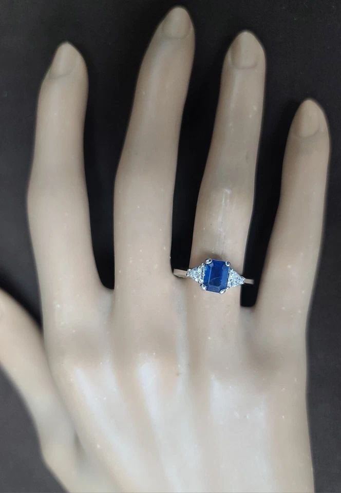 18K White Gold Engagement Ring 1.15CT. Natural Blue Sapphire Emerald Shape: 18K WHITE GOLD ENGAGEMENT RING 1.15CT. NATURAL BLUE SAPPHIRE EMERALD SHAPE This exquisite 18K white gold ring features a stunning 1.15CT natural blue sapphire in an emerald shape, accented with two sp