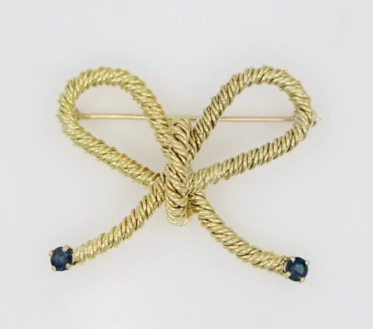 TIFFANY & CO. 18K YELLOW GOLD BLUE SAPPHIRE ROPE BOW TWIST PIN BROOCH 10.1 GR: TIFFANY & CO. 18K YELLOW GOLD BLUE SAPPHIRE ROPE BOW TWIST PIN BROOCH 10.1 GR Description Tiffany & Co. 18K Yellow Gold Blue Sapphire Rope Bow Twist Pin Brooch Pin/brooch is in good condition. May sho