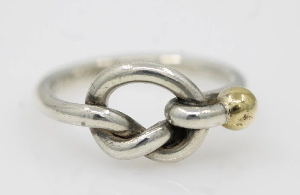 TIFFANY & CO. STERLING SILVER & 18K GOLD LOVE KNOT BAND RING SIZE 5 - 2.9 GRAMS: TIFFANY & CO. STERLING SILVER & 18K GOLD LOVE KNOT BAND RING SIZE 5 - 2.9 GRAMS Description Tiffany & Co. Sterling Silver & 18K Gold Love Knot Band Ring Ring is in good condition. May show signs of we