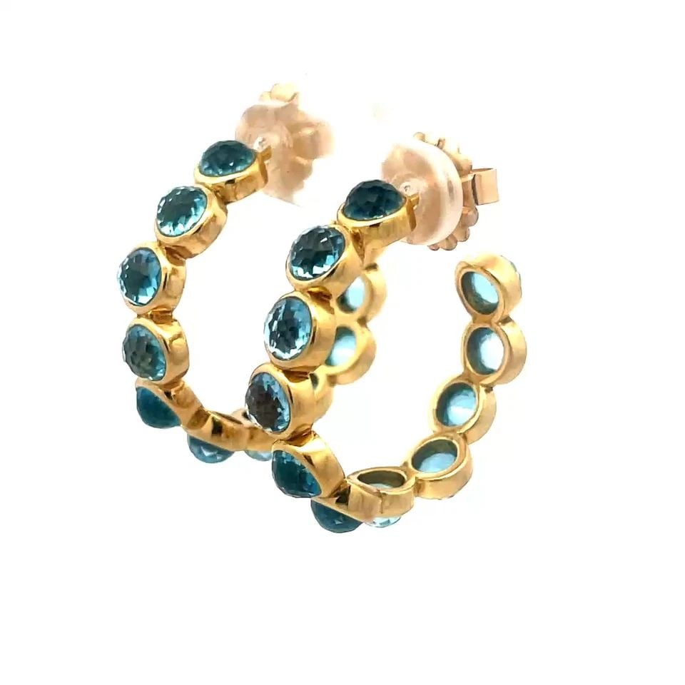 IPPOLITA LILLIPOP GOLD EARRINGS BLUE TOPAZ 18K YELLOW GOLD HOOP STYLE: These charming pair of earrings are by designer Ippolita from the Lollipop Collection. The earrings feature multi-faceted cut bezel set blue topaz stones in 18k yellow gold hoops with 14k yellow gold 