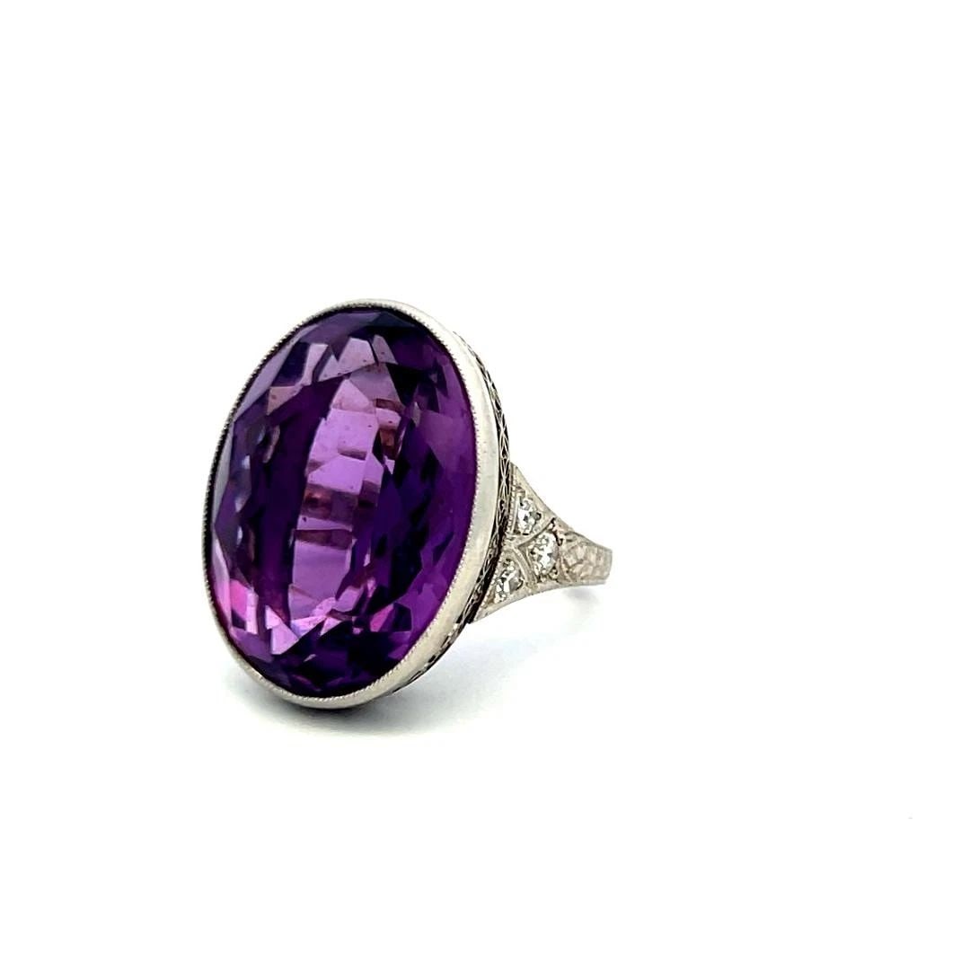 AMETHYST & DIAMOND PLATINUM COCKTAIL RING WITH 18.9-13.6MM OVAL AMETHYST CENTER: AMETHYST & DIAMOND PLATINUM COCKTAIL RING WITH 18.9-13.6MM OVAL AMETHYST CENTER Title: The oval gemstone is bezel-set in a finely detailed platinum mounting, with delicate diamond accents adding a tou