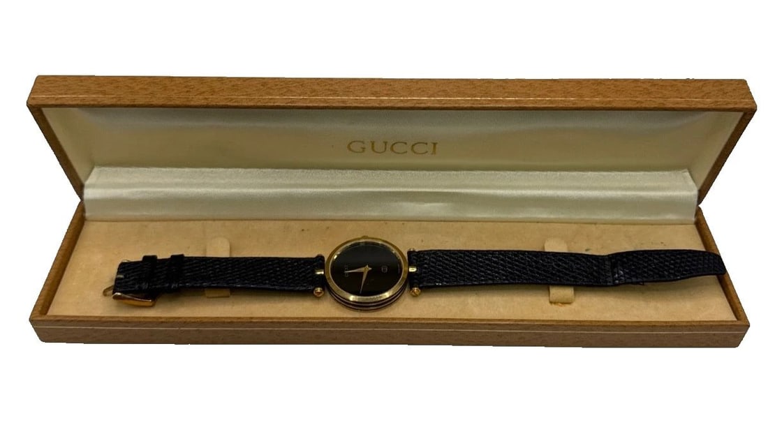 GUCCI SHELLY 30MM QUARTZ WATCH: GUCCI SHELLY 30MM QUARTZ WATCH The Gucci Shelly 30mm Quartz Watch is a stylish unisex wristwatch featuring a black leather two-piece strap and a 30mm round case with a gold plated finish. It boasts a 