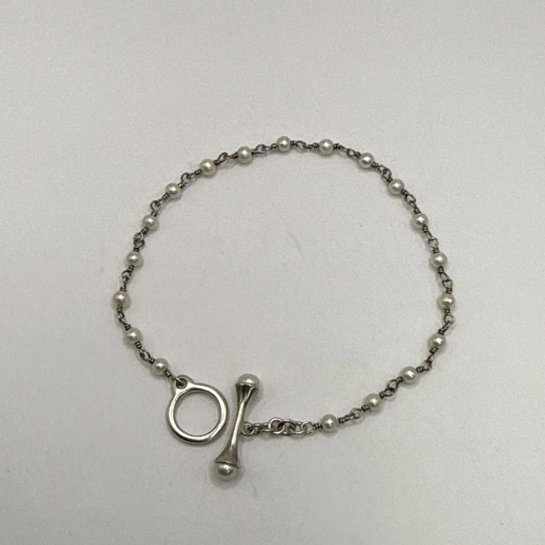 SILVER & FAUX PEARL BRACELET 7": SILVER & FAUX PEARL BRACELET 7" This silver and faux pearl bracelet is a stylish accessory that exudes elegance and sophistication. The bracelet features a chain and beaded style, with a main stone co