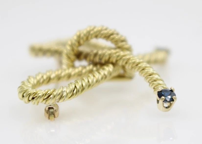 TIFFANY & CO. 18K YELLOW GOLD BLUE SAPPHIRE ROPE BOW TWIST PIN BROOCH 10.1 GR: TIFFANY & CO. 18K YELLOW GOLD BLUE SAPPHIRE ROPE BOW TWIST PIN BROOCH 10.1 GR Description Tiffany & Co. 18K Yellow Gold Blue Sapphire Rope Bow Twist Pin Brooch Pin/brooch is in good condition. May sho
