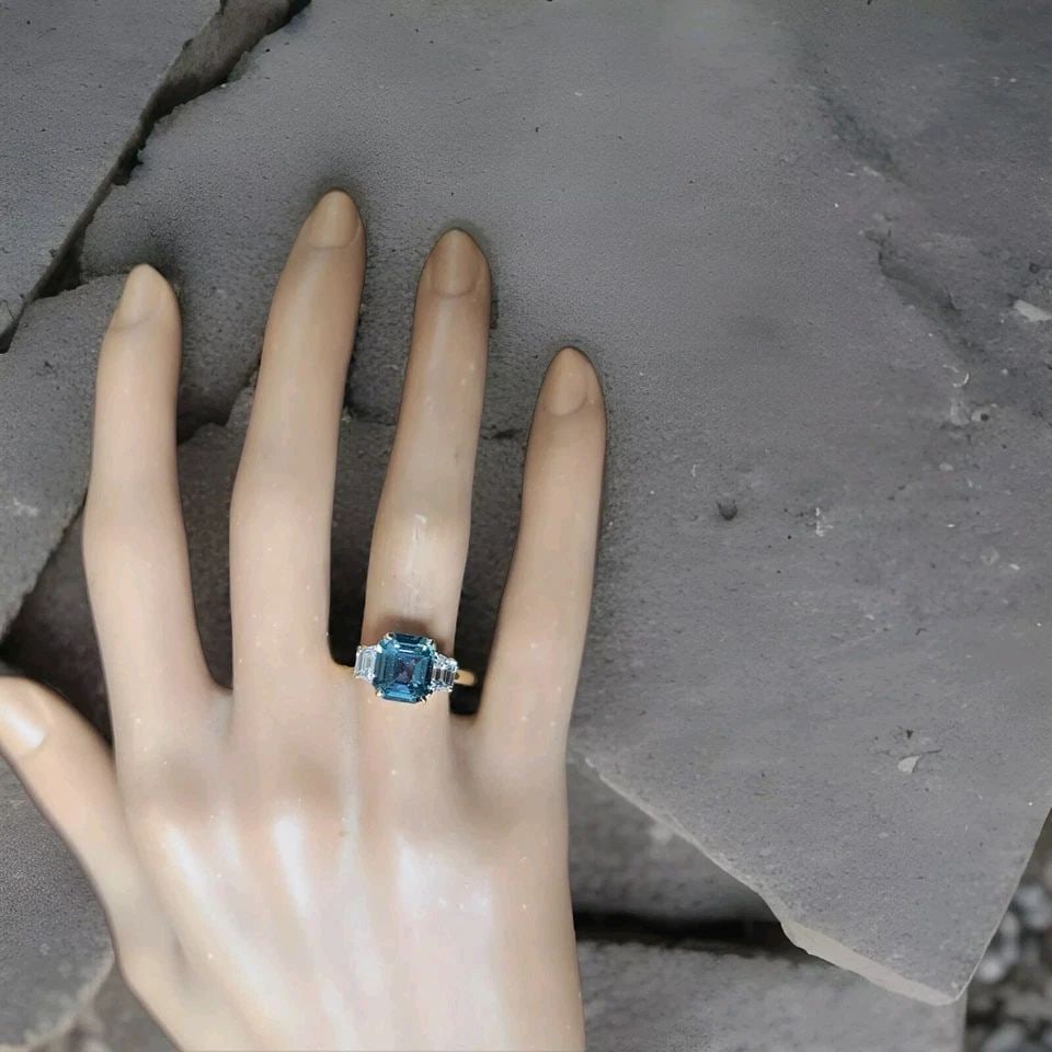 14K YELLOW GOLD ENGAGEMENT RING 2.59CT.UNTREATED TEAL BLUE SAPPHIRE GIA CERT: 14K YELLOW GOLD ENGAGEMENT RING 2.59CT.UNTREATED TEAL BLUE SAPPHIRE GIA CERT This stunning engagement ring features a radiant cut teal blue sapphire as the main stone, with two additional diamonds on 