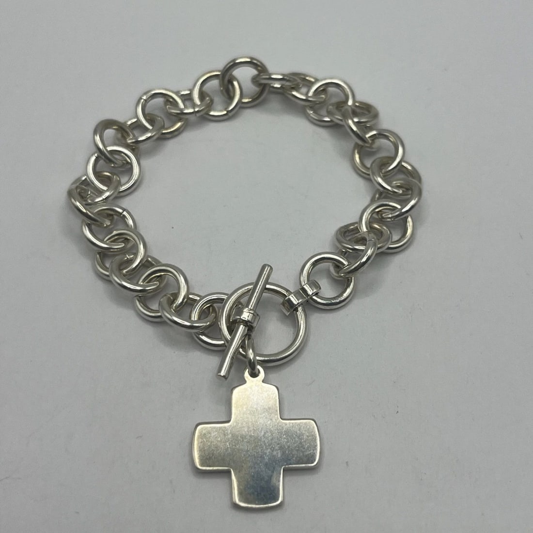 925 7" CIRCLE LINK CHARM BRACELET WITH CROSS & TOGGLE LOCK 26.6 G: 925 7" Circle Link Charm Bracelet with Cross & Toggle Lock 26.6 g This 925 Sterling Silver bracelet features a 7-inch circle link design with a charming cross pendant. The bracelet is secured with a t