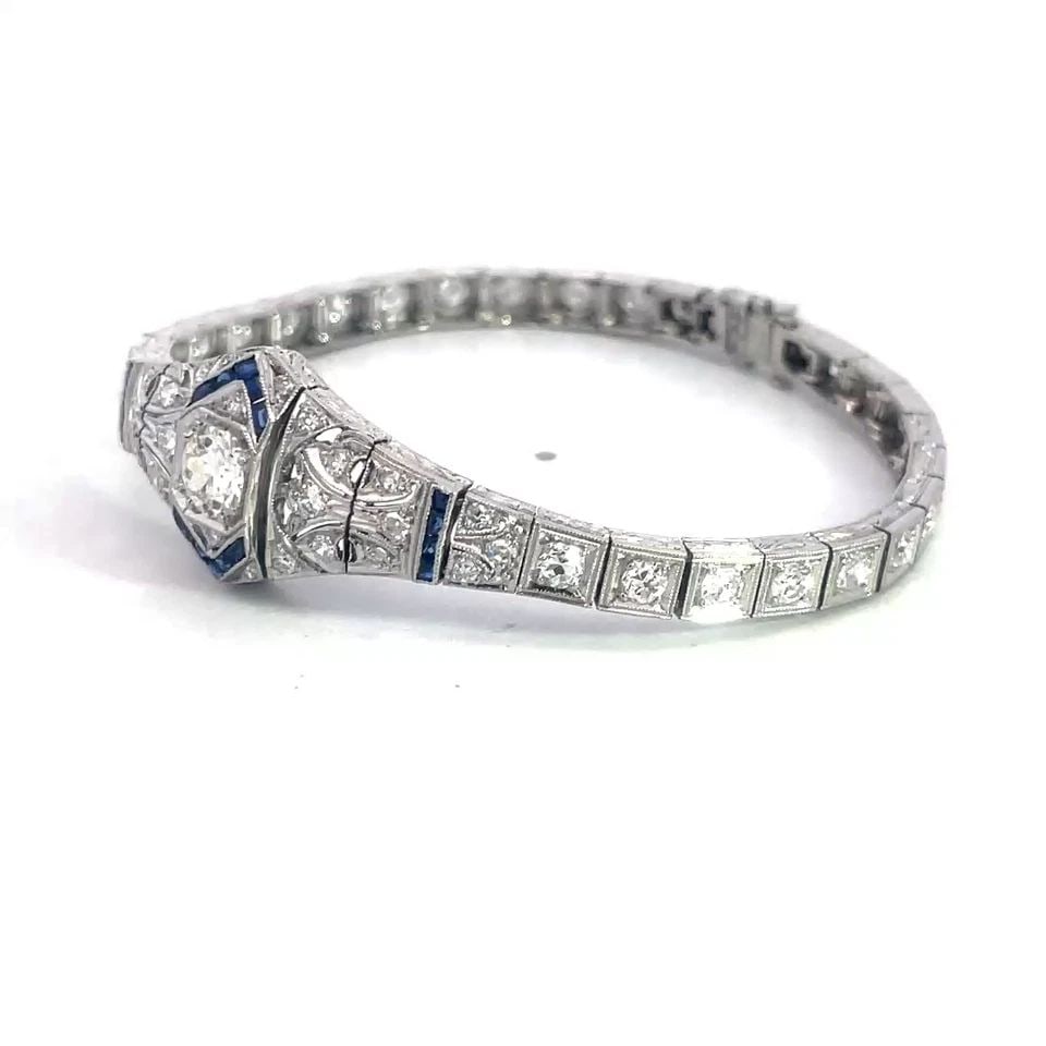 PLATINUM ART DECO BRACELET 3.5CT DIAMOND FLORAL CENTERPIECE CUBE LINKS: The platinum Art Deco bracelet is a stunning piece of antique jewelry featuring a floral centerpiece with a sparkling diamonds accented with blue colored stones, the milgrain filigree asymmetrical sha
