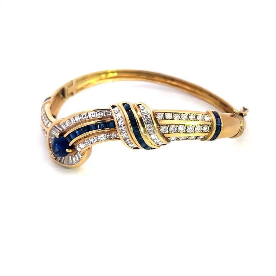 DIAMOND SAPPHIRE GOLD BRACELET 18K YELLOW CURVED HINGE DESIGN BANGLE: This stunning bracelet is crafted from 18k yellow gold featuring the front half in a fancy curved style with a pear shape head pointing down set with baguette diamonds, the center has a pear shape sap