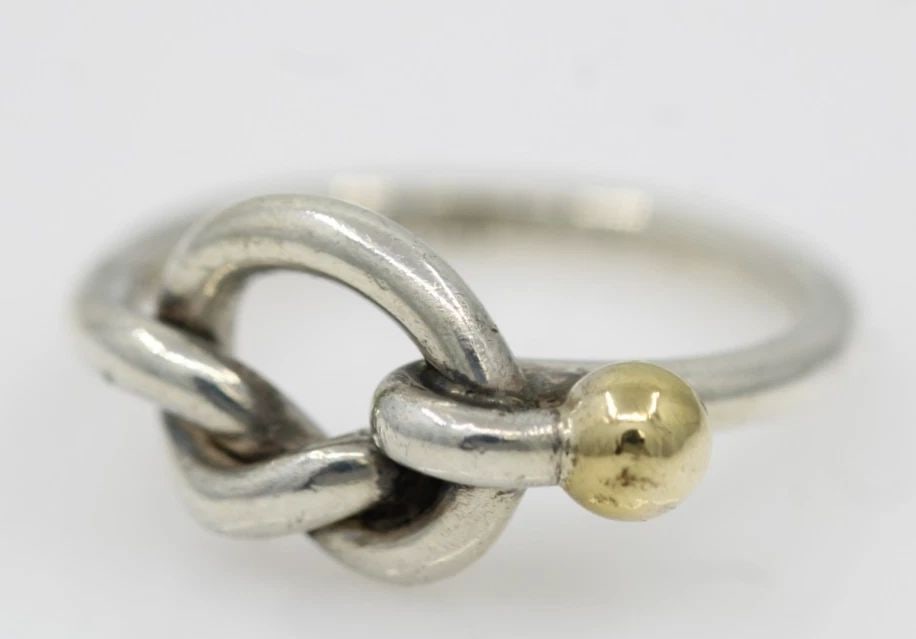 TIFFANY & CO. STERLING SILVER & 18K GOLD LOVE KNOT BAND RING SIZE 5 - 2.9 GRAMS: TIFFANY & CO. STERLING SILVER & 18K GOLD LOVE KNOT BAND RING SIZE 5 - 2.9 GRAMS Description Tiffany & Co. Sterling Silver & 18K Gold Love Knot Band Ring Ring is in good condition. May show signs of we