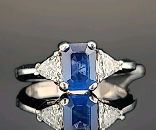 18K WHITE GOLD ENGAGEMENT RING 1.15CT. NATURAL BLUE SAPPHIRE EMERALD SHAPE: 18K WHITE GOLD ENGAGEMENT RING 1.15CT. NATURAL BLUE SAPPHIRE EMERALD SHAPE This exquisite 18K white gold ring features a stunning 1.15CT natural blue sapphire in an emerald shape, accented with two sp